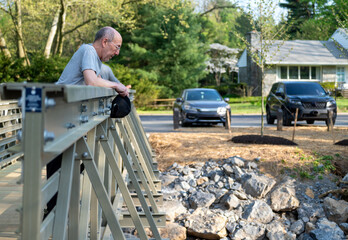 Sad pensive senior man leans over a bridge outdoors in spring summer suburban community park. Mental health illness loss grief concepts, as well as loneliness aging in community old age depression