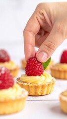 Hand Decorating Miniature Tart with Cream and Fresh Raspberry Over White Table Surface