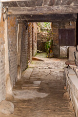 Fototapeta premium A narrow cobbled alley with brick walls and plants, leading to a tranquil courtyard, showcasing traditional architecture and serene ambiance.