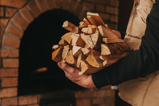 Solid natural heating fuel. man with an armful of firewood near the stove