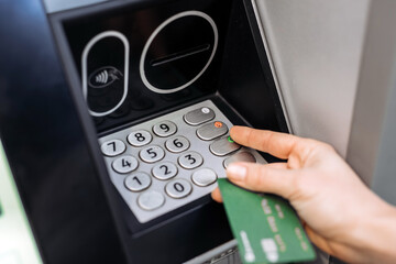 Hand of a person using an ATM machine, entering a PIN code on the keypad, with a bank card in the other hand, illustrating modern banking technology and convenience