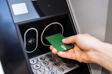 Hand inserting green card into ATM machine, showcasing modern banking technology, with numeric keypad visible, emphasizing convenience and accessibility in financial transactions