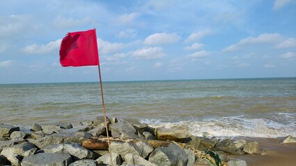Simple and serene view of a bright blue sky partially covered by light, fluffy white clouds with red flag for danger sign of the ocean
