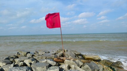 Simple and serene view of a bright blue sky partially covered by light, fluffy white clouds with red flag for danger sign of the ocean