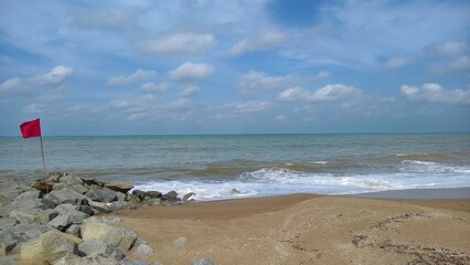 Coastal view featuring large grey rocks on a sandy shore with white waves crashing against the shoreline