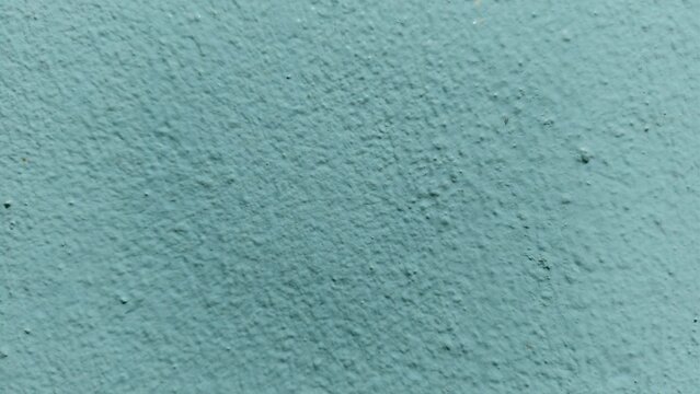 Brightly lit view of a pale blue textured wall displaying small debris particles and minor surface imperfections.