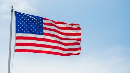 Obraz premium American Flag Waving in the Wind Against a Clear Blue Sky Background