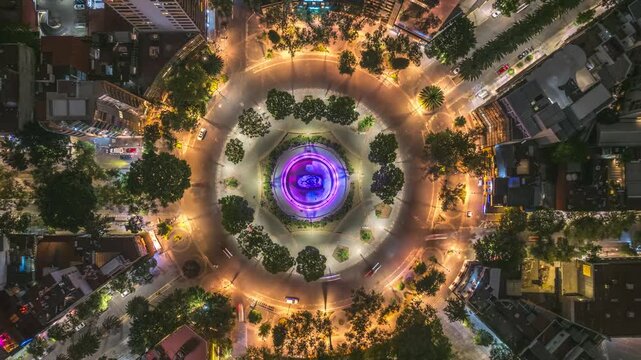 Top-down night hyperlapse descending over the illuminated Fuente de Cibeles, capturing circular traffic patterns and the urban grid glowing around the landmark in Mexico City.