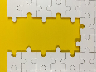 A minimalist high-angle shot of white jigsaw puzzle pieces on a vibrant yellow background, featuring a large central gap perfect for copy or custom concepts.