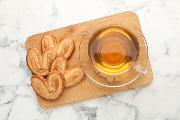 Palmiers and cup of tea on marble table, top view. Puff pastry cookies