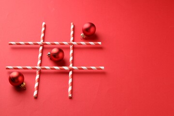 Tic tac toe game made with Christmas balls on red background. Space for text