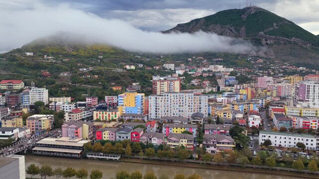 Aerial video of Lezh&euml;, Albania with fog sliding over the hillside rising above colourful city blocks.