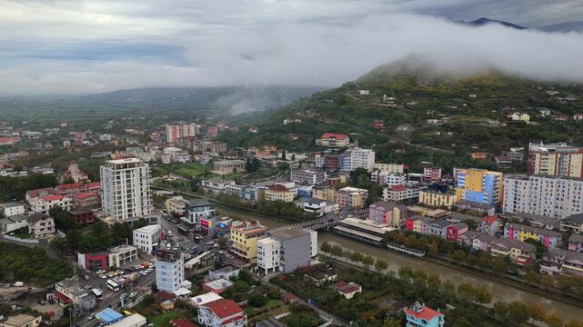 Aerial video of Lezh&euml;, Albania with fog sliding over the hillside rising above colourful city blocks.