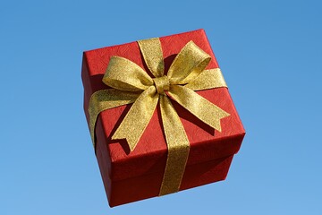 A vibrant red gift box with a sparkling gold bow floats against a clear blue sky