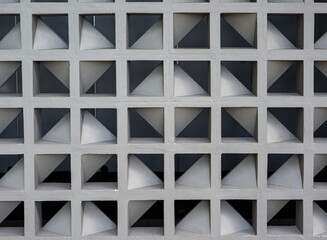 A grey concrete breeze block wall featuring a repetitive geometric grid pattern of square and triangular cutouts.