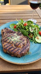 juicy grilled steak with charred grill marks on a blue plate beside fresh mixed green salad