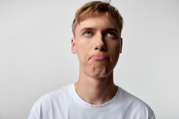 Young man expression thinking pensive confusion gaze upward look white t shirt studio lighting calm mood emotion image candid minimal background neutral tones indoor light focus on facial features