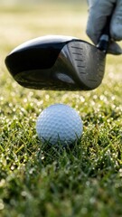 closeup of a golf ball resting on dewy grass with a driver poised to strike hour