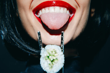 Playful woman with red lips holding sushi with chopsticks in a fun and vibrant culinary portrait.