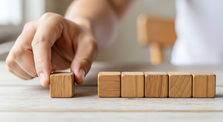 Hand placing wooden block in a row of cubes on a table image