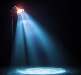 Naklejka premium single stage spotlight on a tall stand casting blue beams through haze onto a circular lit patch on a dark stage, evoking drama and lonely anticipation