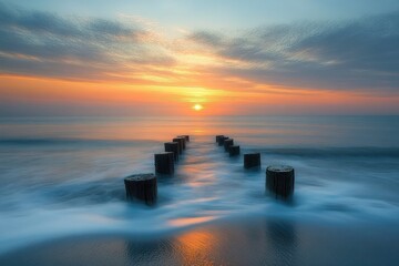 Tranquil coastal sunrise with weathered wooden posts leading into silky surf and a glowing orange sun reflected on calm water