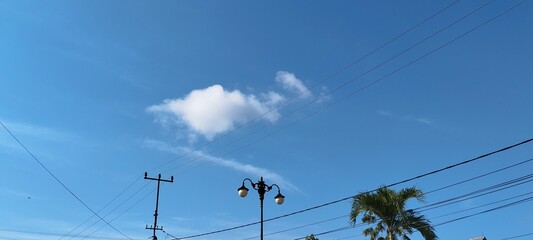 A fluffy white cloud floating above a street lamp and wires