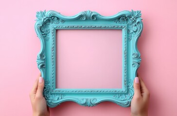 two manicured hands holding an ornate turquoise square picture frame against a pastel pink background, playful feminine creative mood