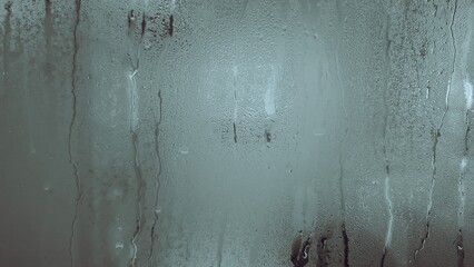Window pane covered in condensation and raindrops, creating a blurred, abstract surface