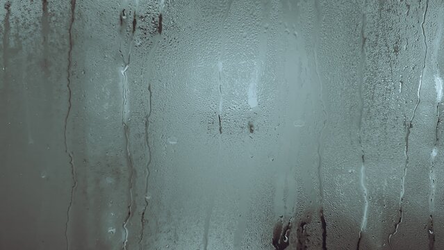 Window pane covered in condensation and raindrops, creating a blurred, abstract surface
