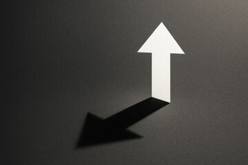 Simple white arrow pointing upwards with a contrasting shadow on dark textured surface arrow.