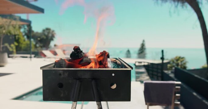 Empty, pool and bbq with flames in backyard for party, holiday and lunch on weekend outdoor. Cookout, barbecue and grill with fire, wood and heat at house for smoke, celebration and vacation
