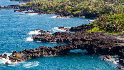 Aerial View of natural arch at black sand beach state park along road to Hana coastal town with surrounding lush green forest in Maui, Hawaii landscape 
