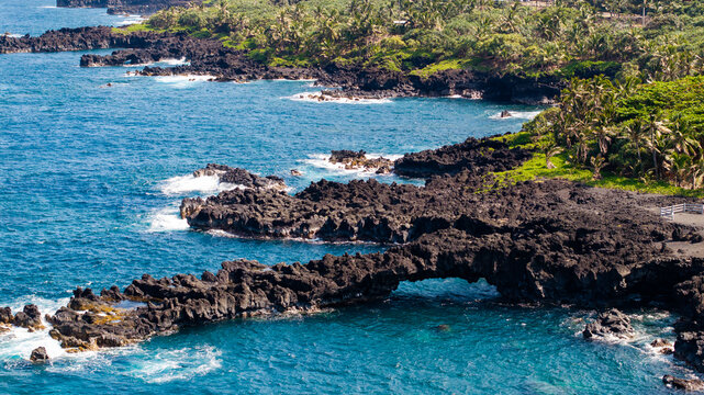 Aerial View of natural arch at black sand beach state park along road to Hana coastal town with surrounding lush green forest in Maui, Hawaii landscape 