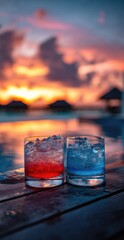 Two vibrant cocktails, red and blue, sit on a wooden surface by a pool, bathed in the warm hues of a beautiful sunset.