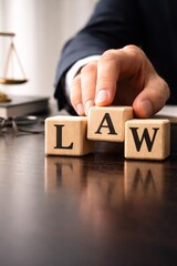 Hand placing wooden letter blocks spelling LAW on dark desk symbolizing legal authority and justice