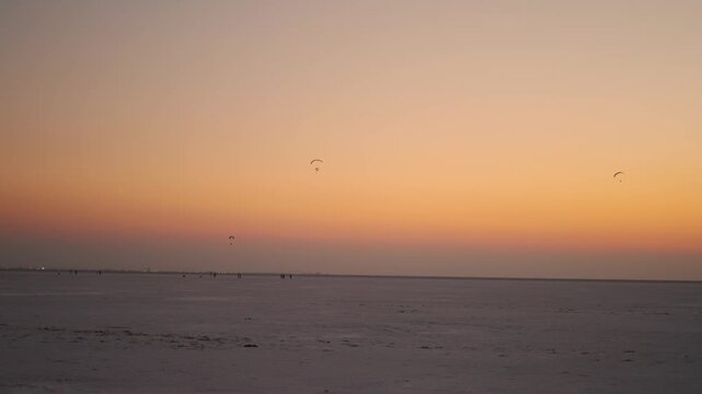 4K shot of sunset at the Rann of Kutch during the winter season with people enjoying paragliding in the sky as seen from Kutch in Gujarat, India. Scenic view of sunset at White desert in Kutch region.