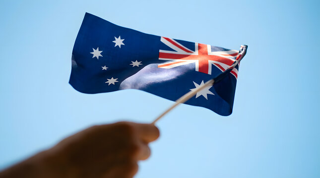 Australia day a hand holds a small australian flag with stars and the union jack against a clear light blue sky background