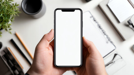 A person holding a smartphone with a blank screen, surrounded by office supplies, perfect for showcasing mobile apps.