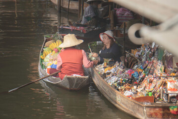 Obraz premium Local fruit vendor rowing a boat at a traditional Thai floating market.
