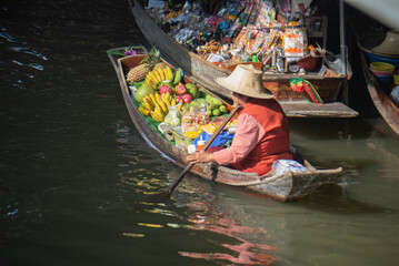 Obraz premium Local fruit vendor rowing a boat at a traditional Thai floating market.