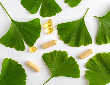 Natural herbal supplement capsules with green ginkgo biloba leaves on a white background. Concept of organic medicine