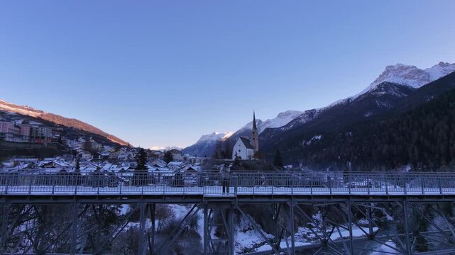 Man Walking Across Icy Bridge in Swiss Alpine Village During Winter &ndash; Snowy Mountains, Rural Switzerland and Cold Seasonal Atmosphere