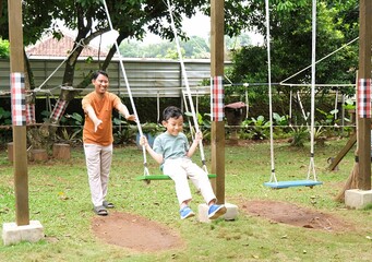 A father gently encouraging his son while playing on a swing in a natural outdoor playground. Highlights active parenting, healthy childhood, and sustainable play environments.