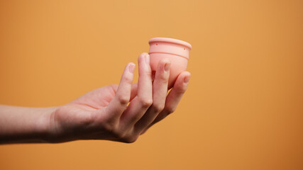 Female Hand Holding Menstrual Cup on Orange Background Minimal Hygiene