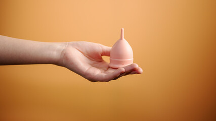 Female Hand Holding Menstrual Cup on Orange Background Minimal Hygiene