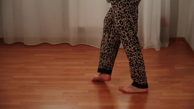 Woman dances at home in leopard print pajamas during daytime hours
