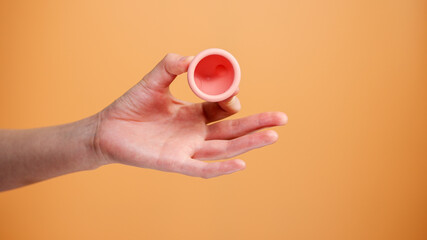 Female Hand Holding Menstrual Cup on Orange Background Minimal Hygiene