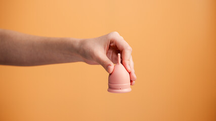 Female Hand Holding Menstrual Cup on Orange Background Minimal Hygiene