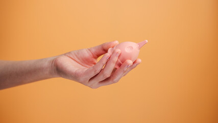 Female Hand Holding Menstrual Cup on Orange Background Minimal Hygiene